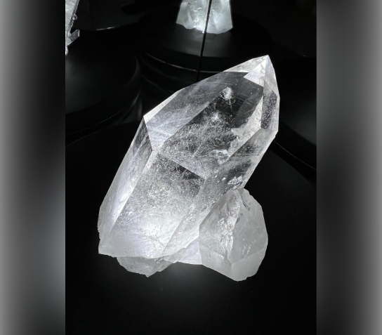 A large clear quartz crystal with a pointed tip on a dark background.