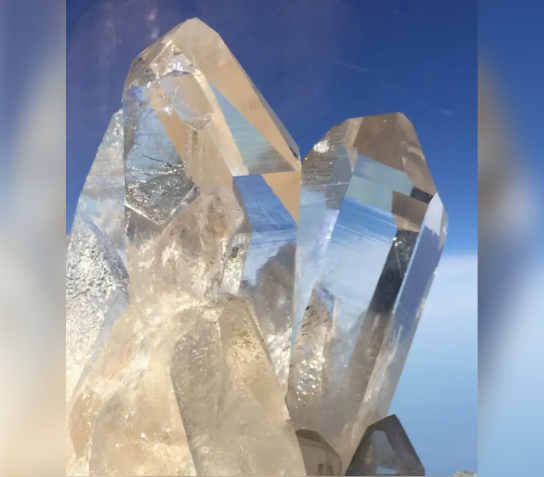 Clear quartz crystals reflecting light against a blue background.
